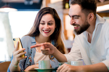 Two people using a mobile phone together at a coffee shop.
