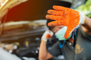Hands of a mechanic wearing orange gloves inspecting a car.