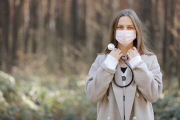 portrait of young woman in a face protective mask- girl with stethoscope around the neck-image of beautiful lady outdoors. copy space.