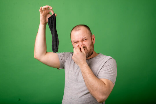 Middle aged man sniffing smelly sock on green background. Laundry, hygiene, smelly feet concept.