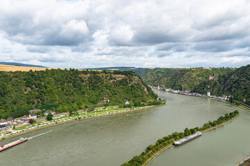 Fototapeta na wymiar The river Rhine in western Germany flows between the hills covered with forest, visible barge and rock cliff.
