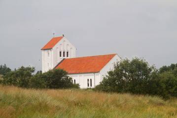 Nørre Lyngvig church, a typical Danish church, white with red tiled roof, between trees and dunes
