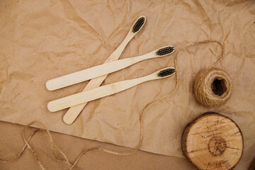 Three toothbrushes made of natural bamboo are lying on a piece of wood, against a background of brown kraft paper.
