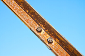 Old rusty iron structure with bolted metal profiles against a blue sky