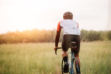 A man ride on bike on the road. Man riding vintage sports bike for evening exercise. A man ride bicycle to breathe in the fresh air in midst of nature, meadow, forest, with evening sun shining through