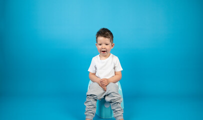 Full-length portrait of a yawning toddler sitting on a potty, blue background with copy space.
