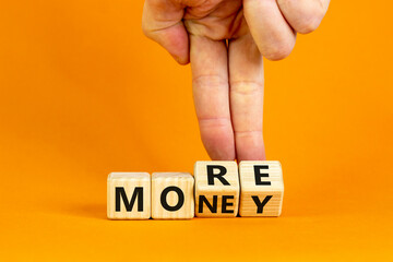 More money symbol. Businessman turns wooden cubes and changes the word 'More' to 'Money'. Beautiful orange table, orange background, copy space. Business and more money concept.