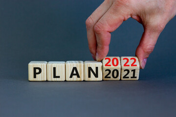 2022 plan new year symbol. Businessman turns a wooden cube and changes words 'Plan 2021' to 'Plan 2022'. Beautiful grey background, copy space. Business, 2022 plan new year concept.