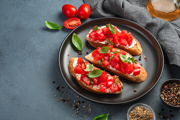 Three bruschetta with tomatoes, basil and cheese on a black plate.