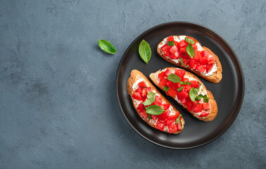 Traditional bruschetta with tomatoes and basil in a black plate on a dark background.