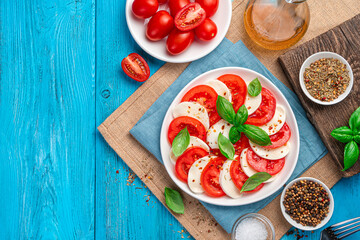 Caprese salad of chopped fresh tomatoes, mozzarella cheese, basil and olive oil on a blue wooden table.