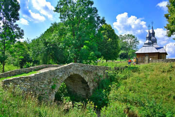Old stone bridge near a wooden orthodox church in village Olchowiec, Low Beskids (Beskid Niski), Poland - obrazy, fototapety, plakaty