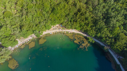 Small round lake full of swimmers sorrounded by trees during a sunny summer day aerial view