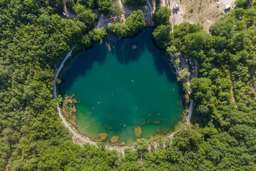 Round small lake sorrounded by trees during a sunny summer day , overhead view