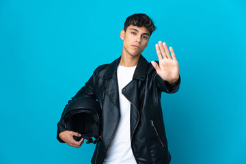 Fototapeta premium Young man with a motorcycle helmet over isolated blue background making stop gesture