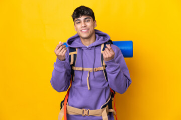 Young mountaineer man with a big backpack over isolated yellow background making money gesture
