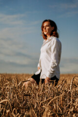 Happy young woman in a white shirt in a wheat field. Sunny day. The girl walks across the field. Blurred background, focus to foreground