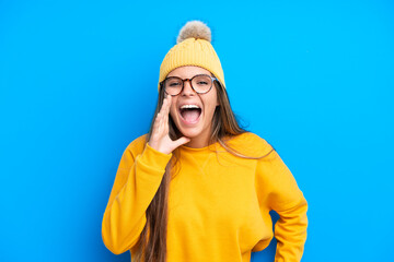 Young caucasian woman wearing winter clothes isolated on blue background shouting with mouth wide open