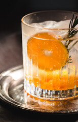 Alcoholic Drink gin and tonic with orange, ice and rosemary sprig on a moody environment
