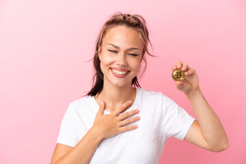 Teenager Russian girl holding a Bitcoin isolated on pink background smiling a lot