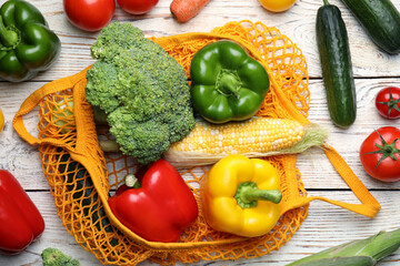 Net bag with different fresh vegetables on white wooden table, flat lay
