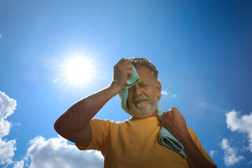 Senior man with towel suffering from heat stroke outdoors, low angle view