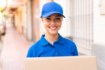 Young delivery woman at outdoors holding boxes with happy expression