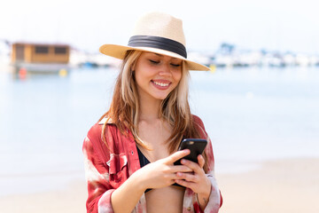 Young pretty woman in summer holidays at beach sending a message with the mobile