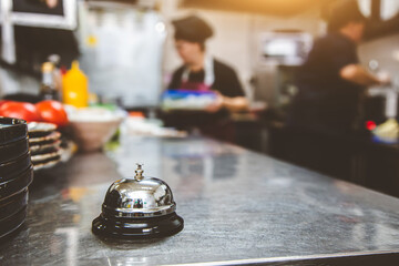 Silver Call Bell on table, chefs in a restaurant on background. cooking in the kitchen.