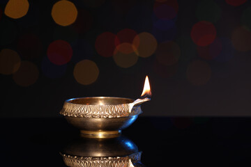 Lit diya on dark background with blurred lights, space for text. Diwali lamp
