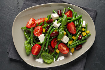 Plate of tasty salad with green beans on black table, top view