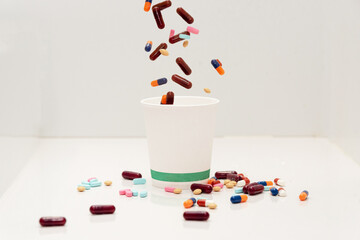 píldoras y pastillas cayendo desde arriba a un vaso de papel con más pastillas y píldoras a su...
