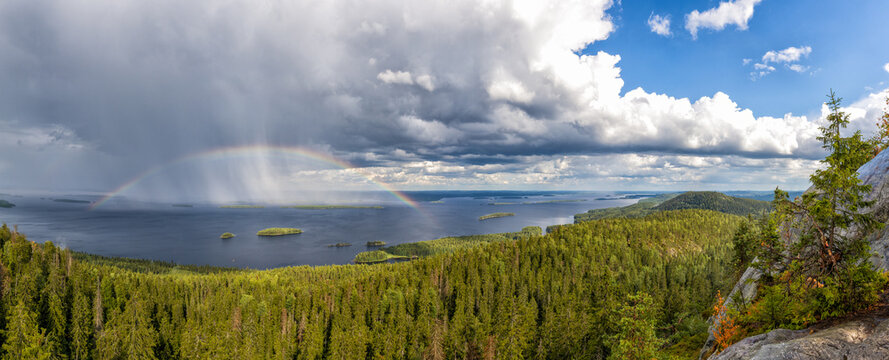 panorama view of Pielina Lake and islands in Koli National Park in Finland with a rainbow under an expressive cloudy sky