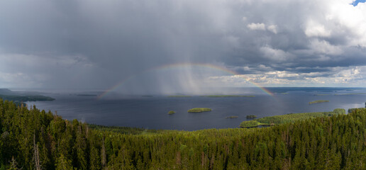 panorama landscape with a colorful rainbow over a deep blue lake with lush green forest and small islands