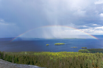 colorful rainbow over a deep blue lake with lush green forest and small islands