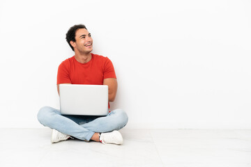 Caucasian handsome man with a laptop sitting on the floor happy and smiling