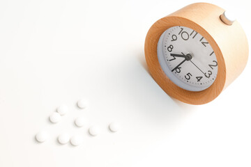Alarm clock and white blue pills on white table background.