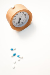 Alarm clock and white blue pills on white table background.