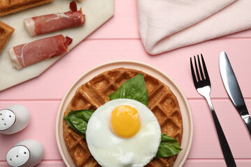 Fresh Belgian waffles with fried egg, basil and jamon served for breakfast on pink wooden table, flat lay