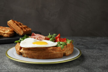 Fresh Belgian waffle with fried egg, arugula, tomatoes and jamon served for breakfast on grey table