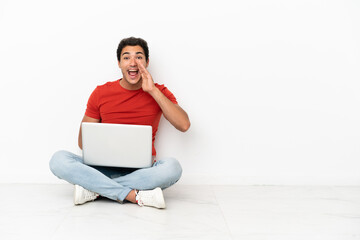 Caucasian handsome man with a laptop sitting on the floor shouting with mouth wide open