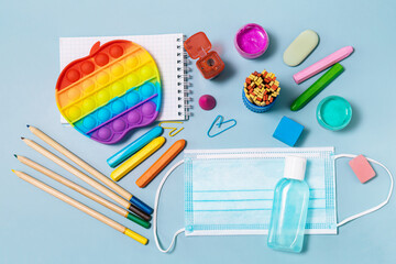 School supplies, poppit anti-stress, face mask, bottle of sanitizer, for back to school on a blue background. Covid-19 precautions. Top view flat lay background.