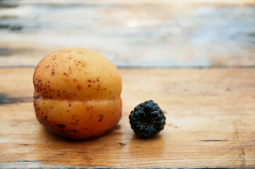 One large apricot and one blackberry lie on a wooden table. High quality photo