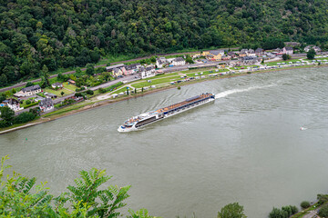 Obraz premium A tourist ship sailing on the river Rhine in western Germany, visible buildings and caravans on the river bank.