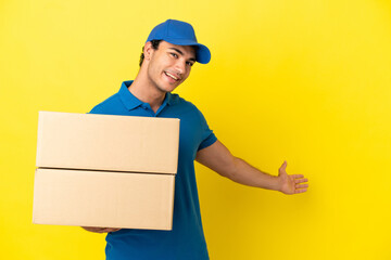 Delivery man over isolated yellow wall extending hands to the side for inviting to come