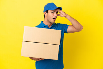 Delivery man over isolated yellow wall doing surprise gesture while looking to the side