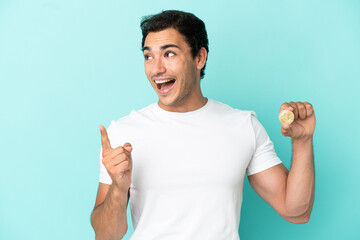 Young man holding a Bitcoin over isolated blue background intending to realizes the solution while lifting a finger up
