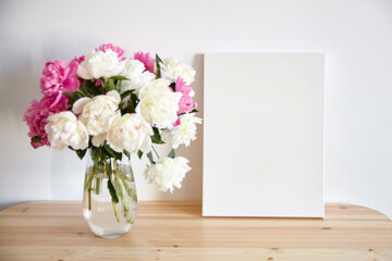 Canvas mockup with pink flowers on wooden table on white wall background