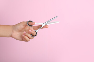 Hairdresser holding professional thinning scissors and space for text on pink background, closeup....