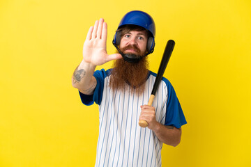 Redhead baseball player man with helmet and bat isolated on yellow background making stop gesture